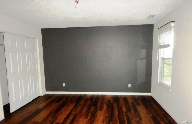 unfurnished room with a textured ceiling, dark wood-type flooring, and a healthy amount of sunlight