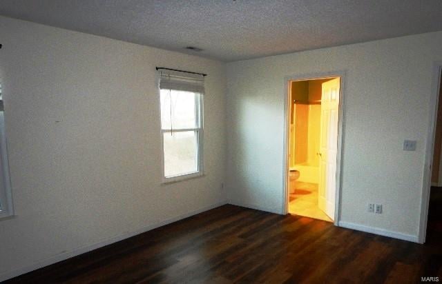 unfurnished bedroom featuring dark hardwood / wood-style flooring, a textured ceiling, and ensuite bath