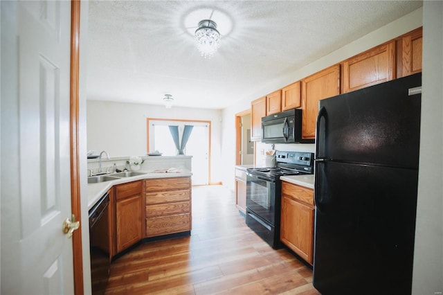 kitchen with black appliances, light hardwood / wood-style flooring, a textured ceiling, and sink