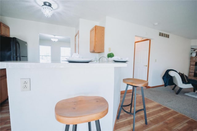 kitchen with kitchen peninsula, light brown cabinetry, black fridge, and wood-type flooring