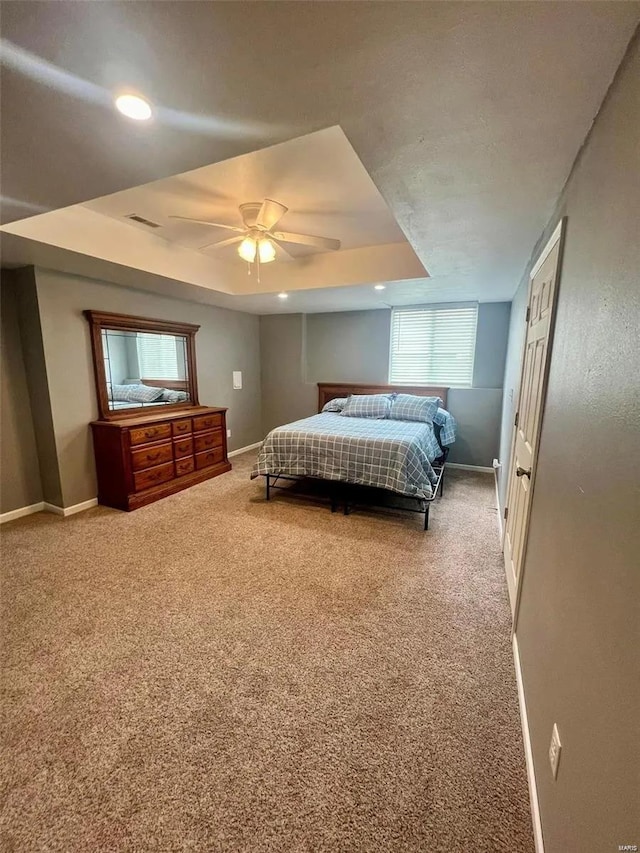 carpeted bedroom with ceiling fan and a raised ceiling