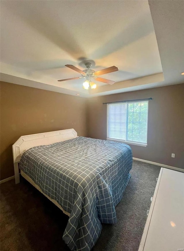 bedroom with dark carpet, a tray ceiling, and ceiling fan