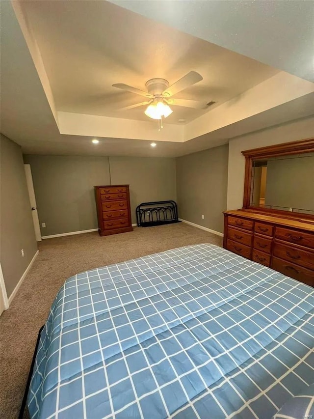 carpeted bedroom with ceiling fan and a tray ceiling