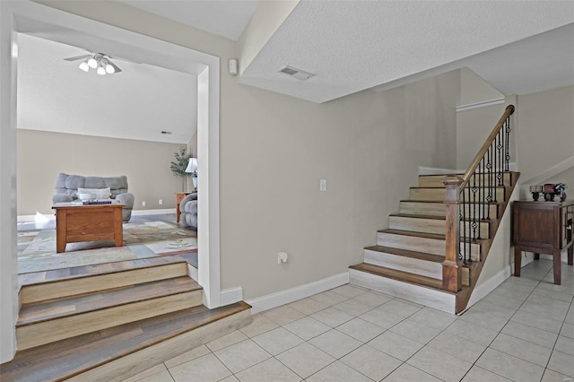 staircase with ceiling fan, tile patterned floors, and a textured ceiling