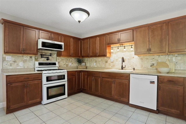 kitchen featuring sink, a textured ceiling, white appliances, and light tile patterned floors