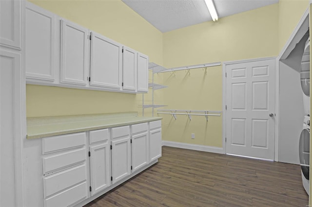 clothes washing area with dark wood-type flooring, stacked washer / dryer, and cabinets