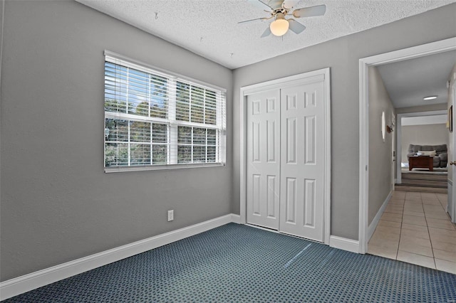 unfurnished bedroom with a textured ceiling, tile patterned flooring, a closet, and ceiling fan