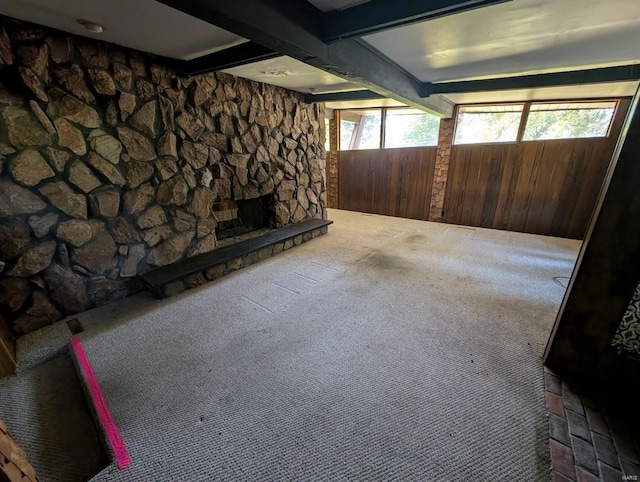 basement with wood walls, carpet floors, a stone fireplace, and a healthy amount of sunlight