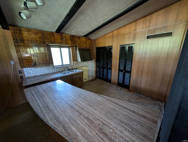 kitchen with a textured ceiling, wood walls, sink, and lofted ceiling with beams