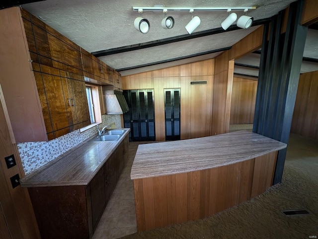 bar featuring sink, a textured ceiling, wooden walls, dark colored carpet, and vaulted ceiling