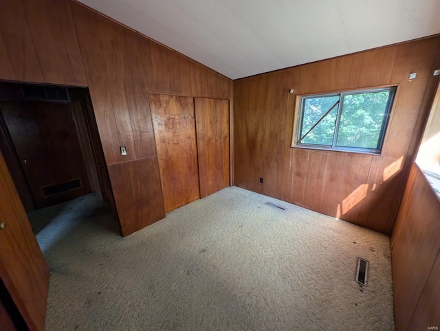 carpeted spare room with wooden walls and vaulted ceiling