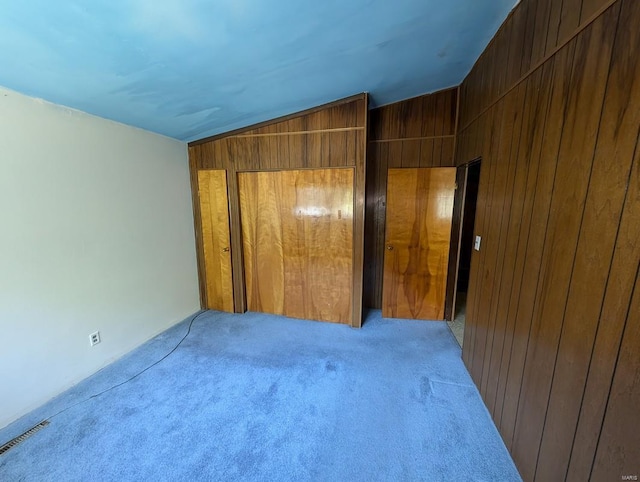 unfurnished bedroom with lofted ceiling, wooden walls, and light carpet