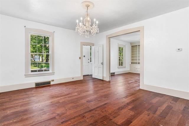 spare room with a notable chandelier, dark hardwood / wood-style floors, and built in features