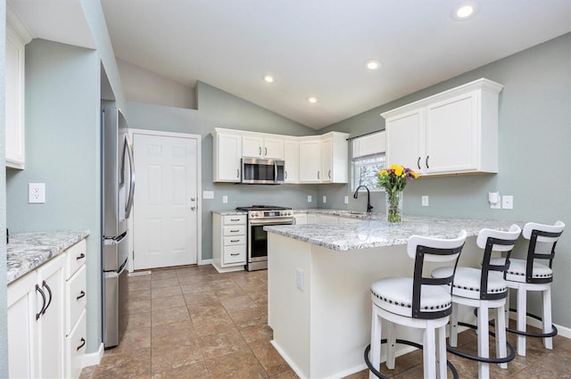 kitchen with kitchen peninsula, lofted ceiling, appliances with stainless steel finishes, white cabinetry, and a kitchen bar