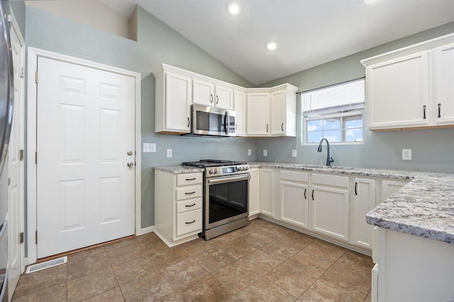 kitchen featuring light stone countertops, sink, stainless steel appliances, vaulted ceiling, and white cabinets