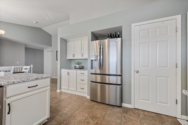 kitchen with white cabinetry, lofted ceiling, stainless steel refrigerator with ice dispenser, and light stone countertops