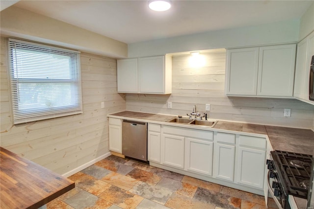 kitchen with wood walls, sink, white cabinetry, stainless steel dishwasher, and gas range