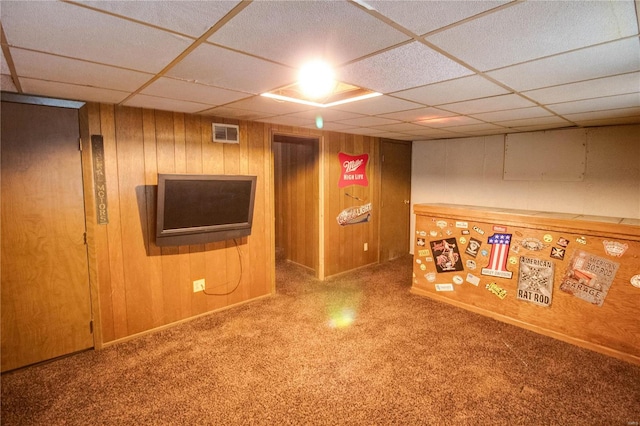 basement featuring a drop ceiling, wooden walls, and carpet