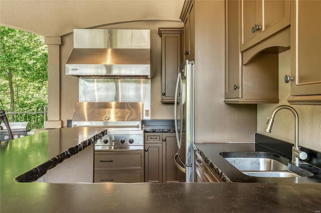 kitchen with dark stone counters, wall chimney exhaust hood, freestanding refrigerator, and a sink