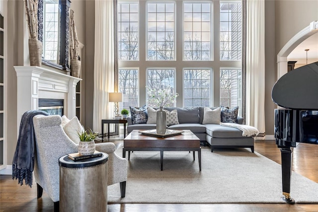 living room with arched walkways, a high ceiling, a healthy amount of sunlight, and wood finished floors