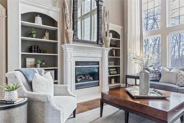 living area featuring built in features, a glass covered fireplace, wood finished floors, and a towering ceiling