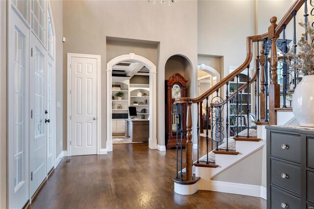 entrance foyer featuring arched walkways, stairway, baseboards, and dark wood-style flooring