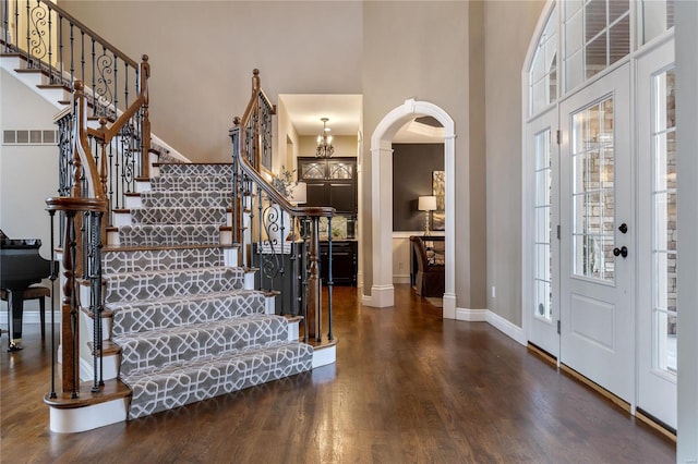 foyer entrance featuring stairway, wood finished floors, visible vents, arched walkways, and a towering ceiling