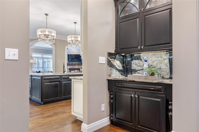 bar with wood finished floors, arched walkways, decorative backsplash, crown molding, and a notable chandelier