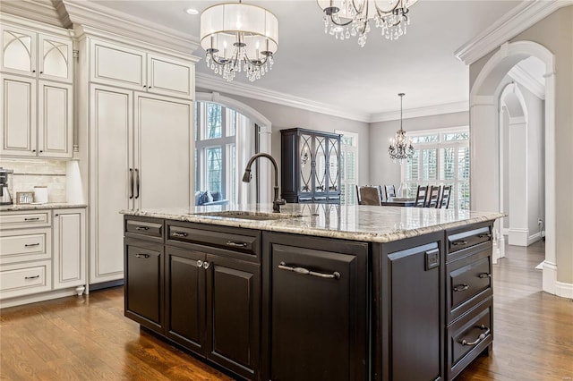 kitchen featuring dark wood finished floors, arched walkways, a sink, crown molding, and a notable chandelier