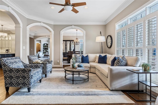 living area with wood finished floors, ceiling fan with notable chandelier, arched walkways, and ornamental molding