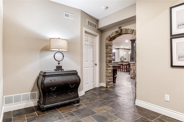 hall featuring arched walkways, visible vents, and baseboards