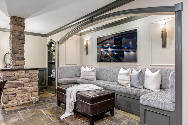 living room with stone tile flooring, arched walkways, crown molding, and decorative columns