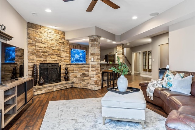 living area with a stone fireplace, wood finished floors, a ceiling fan, and ornate columns