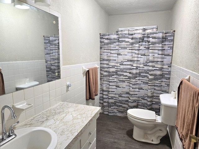 bathroom with a textured ceiling, hardwood / wood-style flooring, tile walls, toilet, and vanity