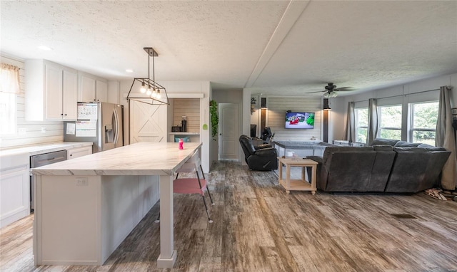 kitchen with white cabinets, wood-type flooring, hanging light fixtures, and stainless steel fridge with ice dispenser