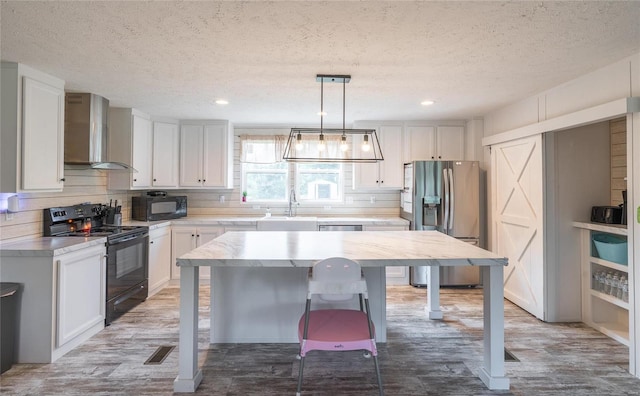 kitchen featuring wall chimney exhaust hood, black appliances, a center island, decorative light fixtures, and white cabinetry