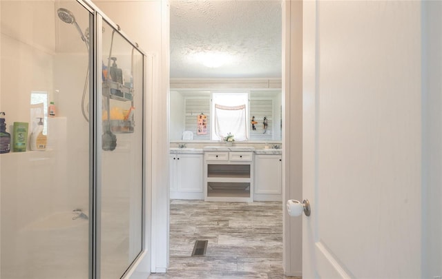 bathroom featuring vanity, a textured ceiling, walk in shower, and wood-type flooring