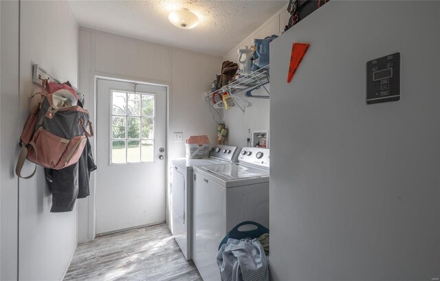 clothes washing area with washer and clothes dryer, a textured ceiling, and light hardwood / wood-style floors