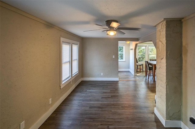 empty room with decorative columns, ornamental molding, dark wood-type flooring, and ceiling fan