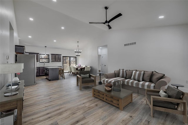 living room with ceiling fan with notable chandelier, lofted ceiling, and light wood-type flooring