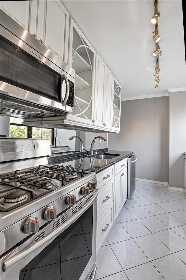 kitchen with stainless steel appliances, dark stone countertops, ornamental molding, sink, and white cabinets