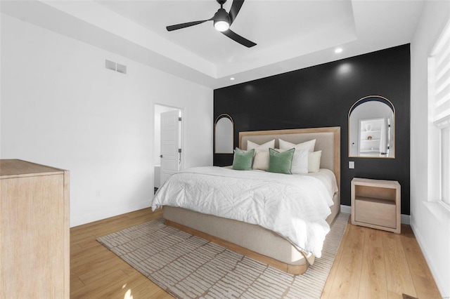 bedroom featuring hardwood / wood-style floors, a raised ceiling, and ceiling fan