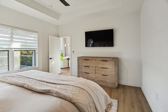 bedroom featuring light hardwood / wood-style floors, a raised ceiling, and ceiling fan