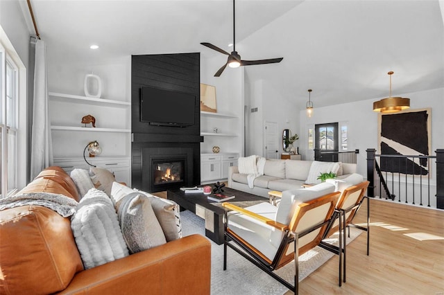 living room with light wood-type flooring, a fireplace, ceiling fan, high vaulted ceiling, and built in shelves