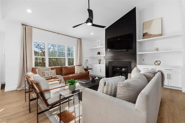 living room with light hardwood / wood-style floors, ceiling fan, a large fireplace, and vaulted ceiling