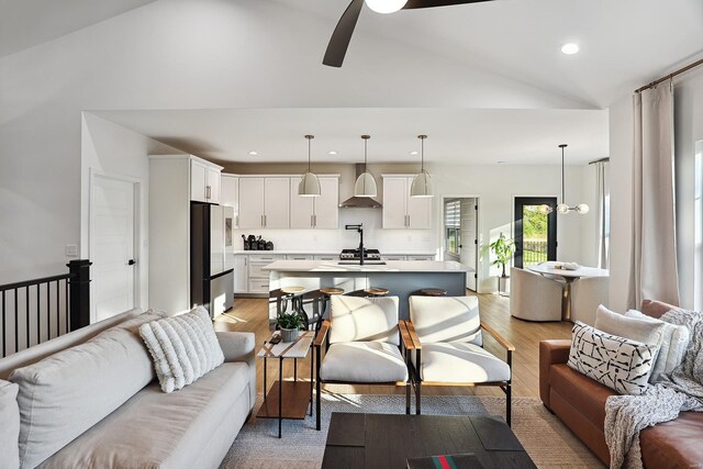 living room with ceiling fan, light wood-type flooring, and vaulted ceiling