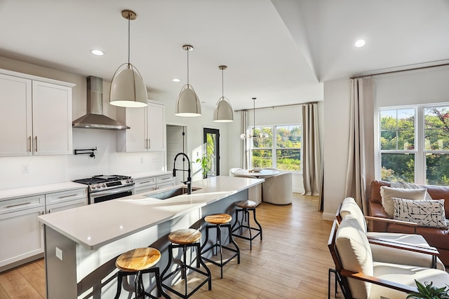 kitchen with sink, light hardwood / wood-style floors, wall chimney range hood, and a healthy amount of sunlight