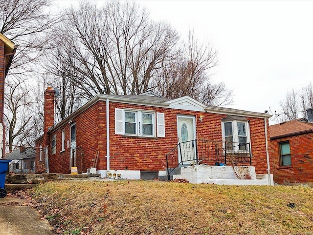 view of front facade with brick siding, a chimney, and a front lawn