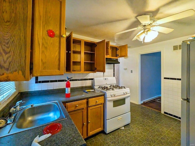 kitchen featuring white gas stove, a sink, open shelves, under cabinet range hood, and freestanding refrigerator