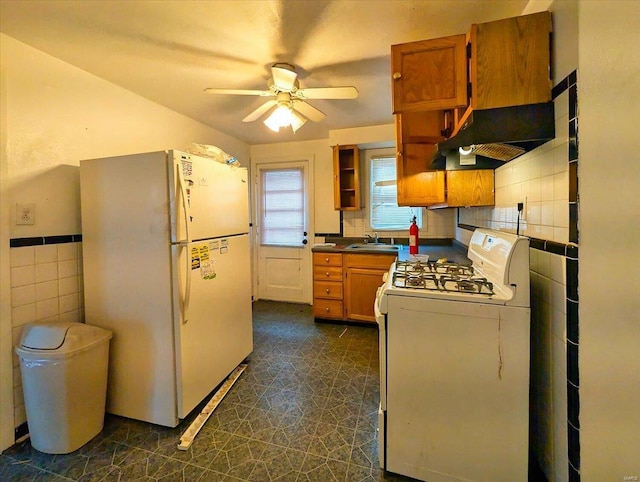 kitchen with brown cabinetry, white appliances, tile walls, a ceiling fan, and a sink